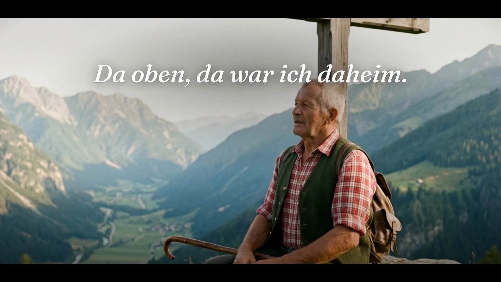 Standbild aus dem Heinz-Spot – ein älterer Mann in kariertem Hemd und Weste sitzt am Gipfelkreuz über einem Alpental, darüber „Da oben, da war ich daheim.“
